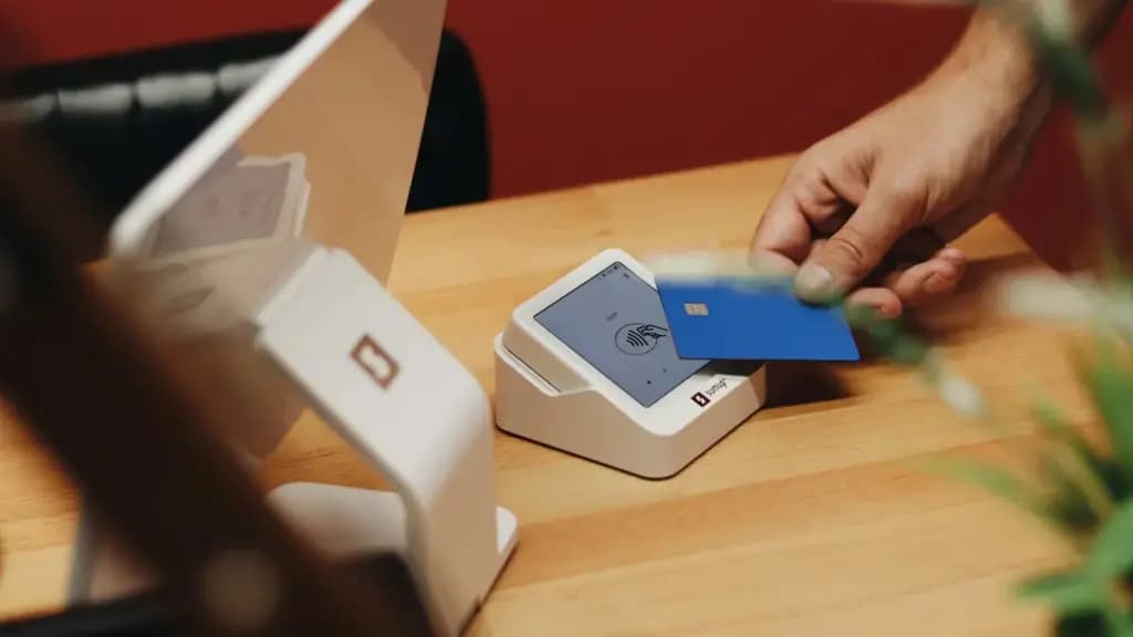 Customer holding a payment card near a card reader on a retail counter.